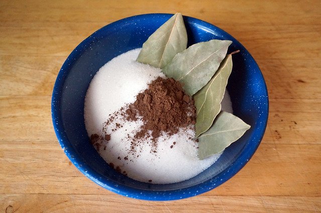 A pile of white sugar in a blue enamel bowl. There are four gray-green sticking out of it like a hedge, and in front of them what looks like a small heap of dirt -- it's actually dark-brown ground allspice.